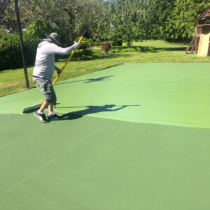 Brush-painting a green acrylic backyard tennis court
